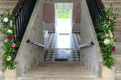 Escalier en pierre décoré de fleurs, menant à une pièce lumineuse avec carrelage en damier et vue sur un jardin.