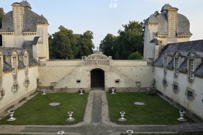 Façade éclairée d'un château à deux tours symétriques, vue de nuit avec des buissons au premier plan.