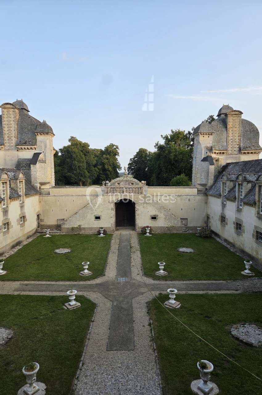 Cour intérieure d'un château avec pelouse, allées gravillonnées, fontaines décoratives et bâtiments en pierre.