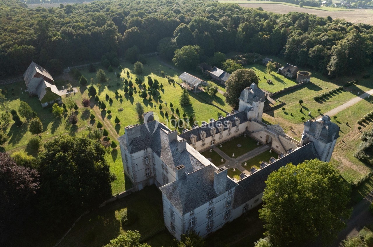 Vue aérienne d'un château entouré de jardins, d'arbres et de bâtiments annexes, au cœur d'une campagne verdoyante.