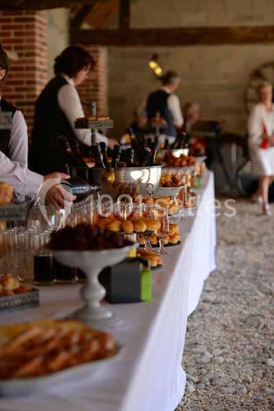 Table de buffet garnie de viennoiseries, boissons et desserts, disposée dans une salle au sol en gravier.