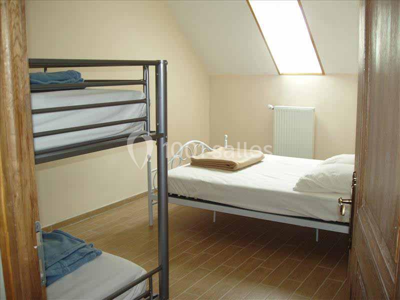 Chambre simple avec lit double, lits superposés, parquet, mur beige et fenêtre de toit laissant entrer la lumière.