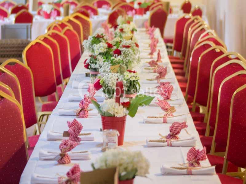 Tables décorées avec des nappes blanches, serviettes pliées et bouquets de fleurs rouges et blanches, entourées de chaises…