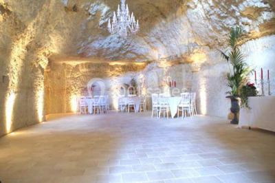 Miniature Location salle Tours (Indre-et-Loire) - La Grotte de la Roche aux Fées #5 Salle décorée dans une grotte avec des tables dressées, chandeliers rouges, plantes vertes et fleurs blanches et rouges.