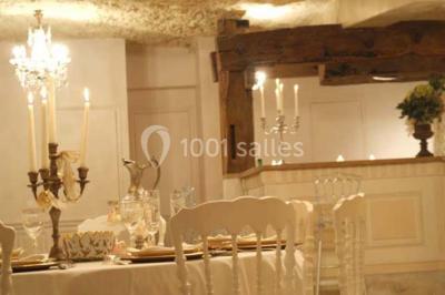 Miniature Location salle Tours (Indre-et-Loire) - La Grotte de la Roche aux Fées #7 Salle décorée dans une grotte avec des tables dressées, chandeliers rouges, plantes vertes et fleurs blanches et rouges.