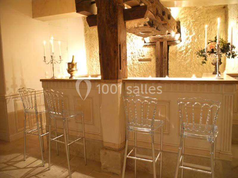 Comptoir de bar en bois clair avec tabourets transparents, éclairé par des bougies et des appliques murales.