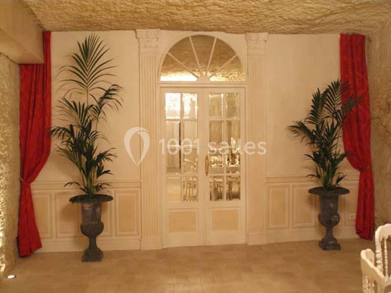 Porte vitrée encadrée de rideaux rouges et de plantes en pot, dans une pièce aux murs clairs et au plafond voûté.