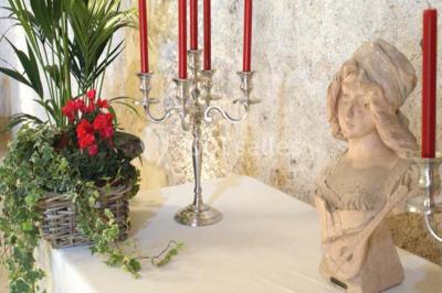 Miniature Location salle Tours (Indre-et-Loire) - La Grotte de la Roche aux Fées #11 Salle décorée dans une grotte avec des tables dressées, chandeliers rouges, plantes vertes et fleurs blanches et rouges.