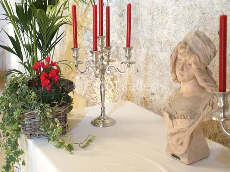 Buste en terre cuite, chandelier argenté avec bougies rouges et plante en pot sur une table recouverte d'une nappe blanche.