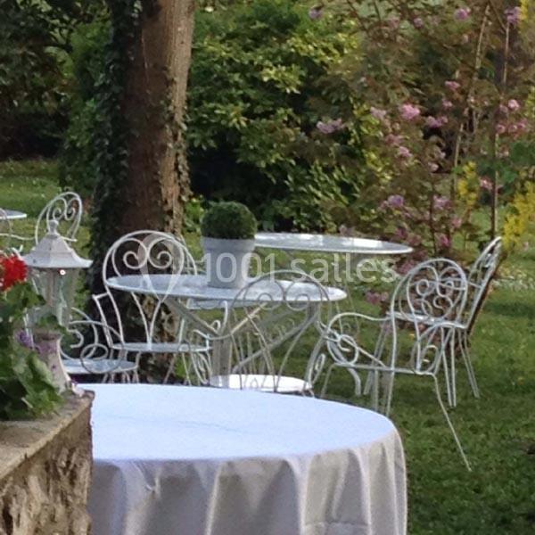 Mobilier de jardin en fer forgé blanc disposé sur une pelouse, entouré de végétation et de fleurs.