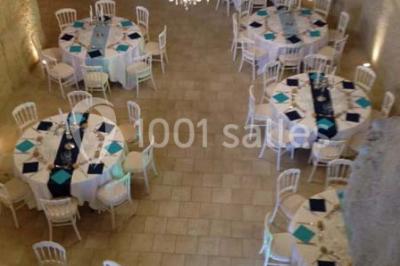 Miniature Location salle Tours (Indre-et-Loire) - La Grotte de la Roche aux Fées #16 Salle décorée dans une grotte avec des tables dressées, chandeliers rouges, plantes vertes et fleurs blanches et rouges.