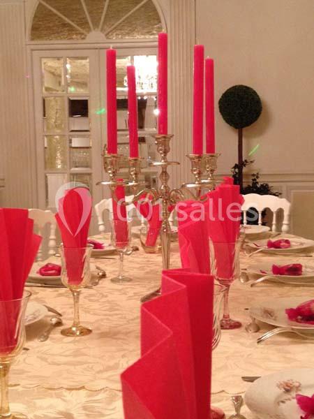 Table élégamment dressée avec nappe beige, serviettes rouges pliées, chandelier argenté et bougies rouges allumées.