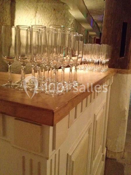 Rangée de flûtes à champagne vides alignées sur un comptoir en bois dans un espace intérieur faiblement éclairé.