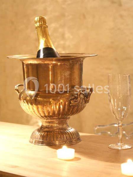 Seau à champagne en métal doré contenant une bouteille, posé sur une table avec une flûte et des bougies allumées.