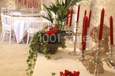 Miniature Location salle Tours (Indre-et-Loire) - La Grotte de la Roche aux Fées #23 Salle décorée dans une grotte avec des tables dressées, chandeliers rouges, plantes vertes et fleurs blanches et rouges.