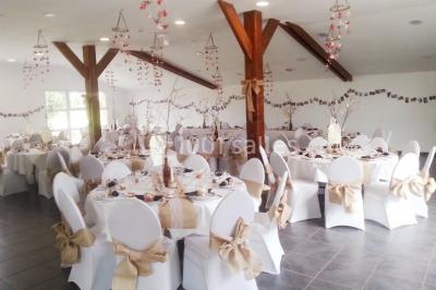 Table ronde décorée pour un événement, avec nappes beige, chaises blanches ornées de tissu orange et centre de table floral.