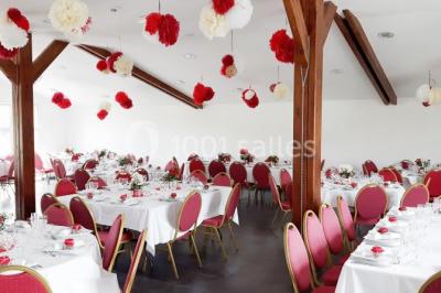 Table ronde décorée pour un événement, avec nappes beige, chaises blanches ornées de tissu orange et centre de table floral.