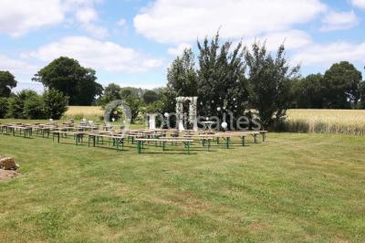 Table ronde décorée pour un événement, avec nappes beige, chaises blanches ornées de tissu orange et centre de table floral.