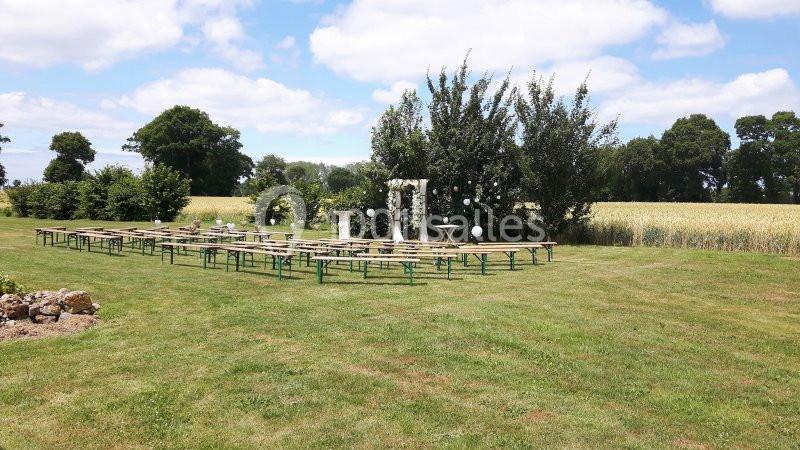 Chaises et tables disposées en extérieur sur une pelouse, avec une arche décorative devant un champ et des arbres.