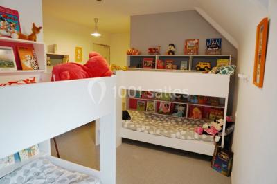 Table ronde décorée pour un événement, avec nappes beige, chaises blanches ornées de tissu orange et centre de table floral.