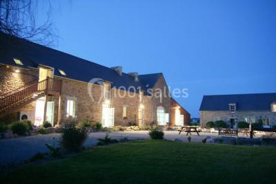 Table ronde décorée pour un événement, avec nappes beige, chaises blanches ornées de tissu orange et centre de table floral.