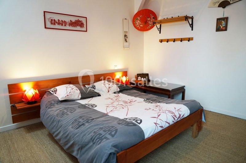 Chambre avec lit double, linge à motifs asiatiques, lampes de chevet rouges et décoration murale d'inspiration japonaise.