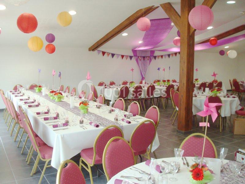 Salle décorée pour un événement avec tables dressées, chaises rouges, lanternes colorées et guirlandes suspendues.