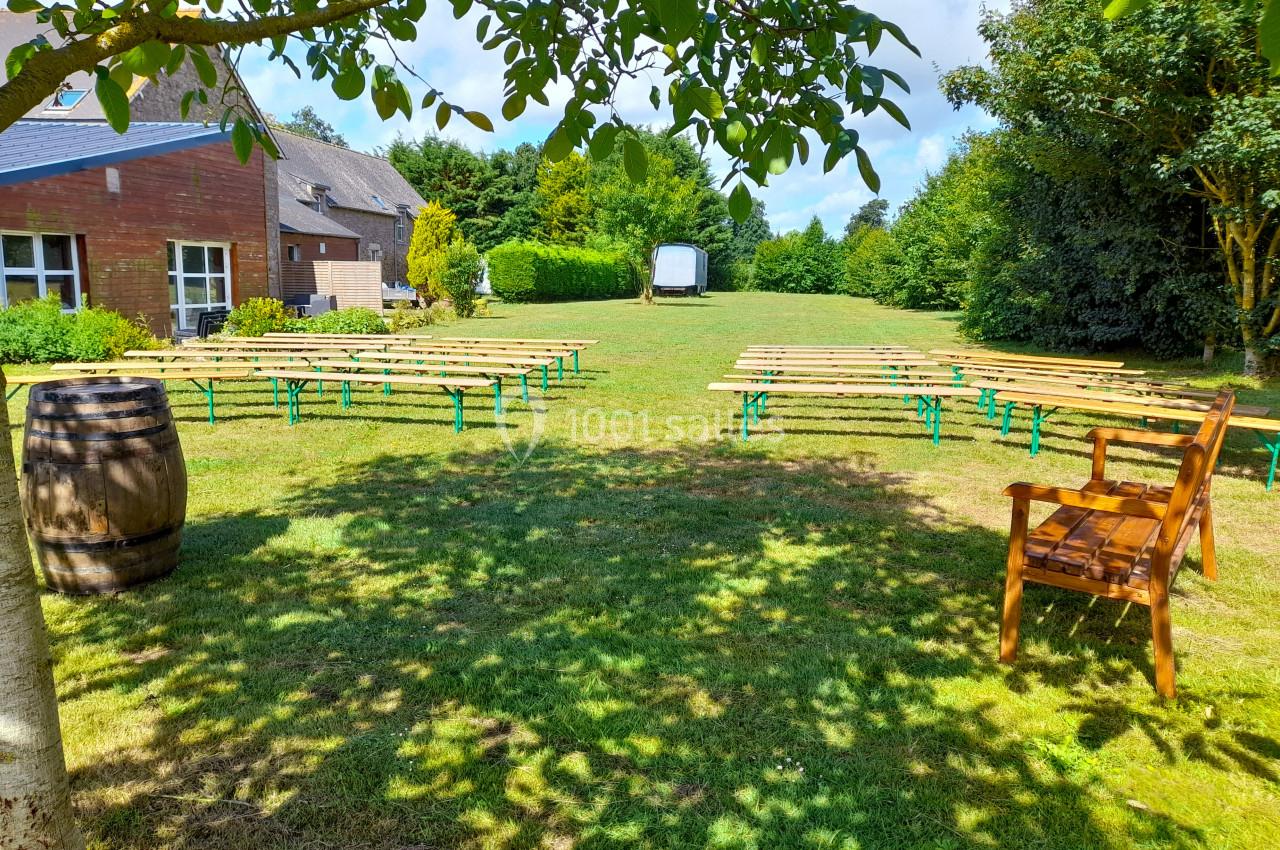 Tables et bancs en bois disposés sur une pelouse, entourés d'arbres, avec un bâtiment en arrière-plan.