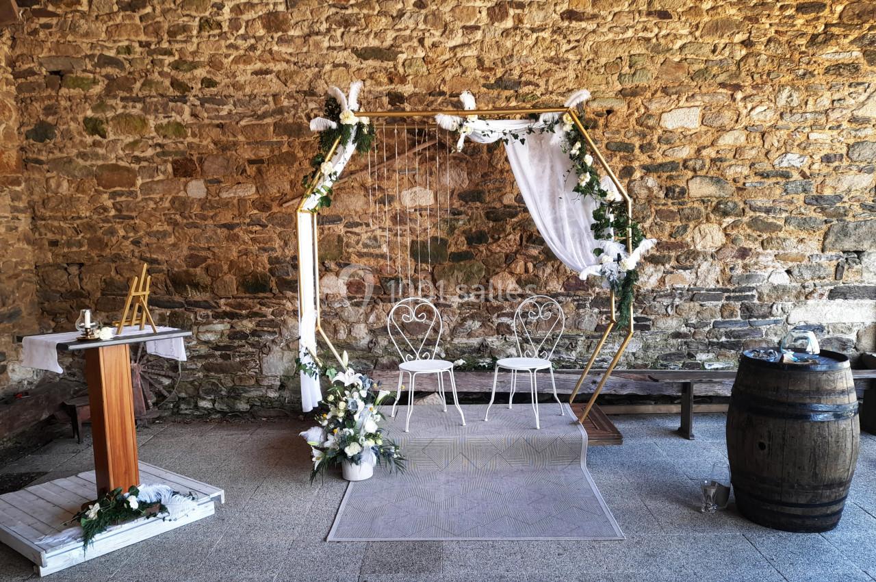 Décor de cérémonie avec arche hexagonale ornée de fleurs blanches, deux chaises et un pupitre en bois devant un mur en…