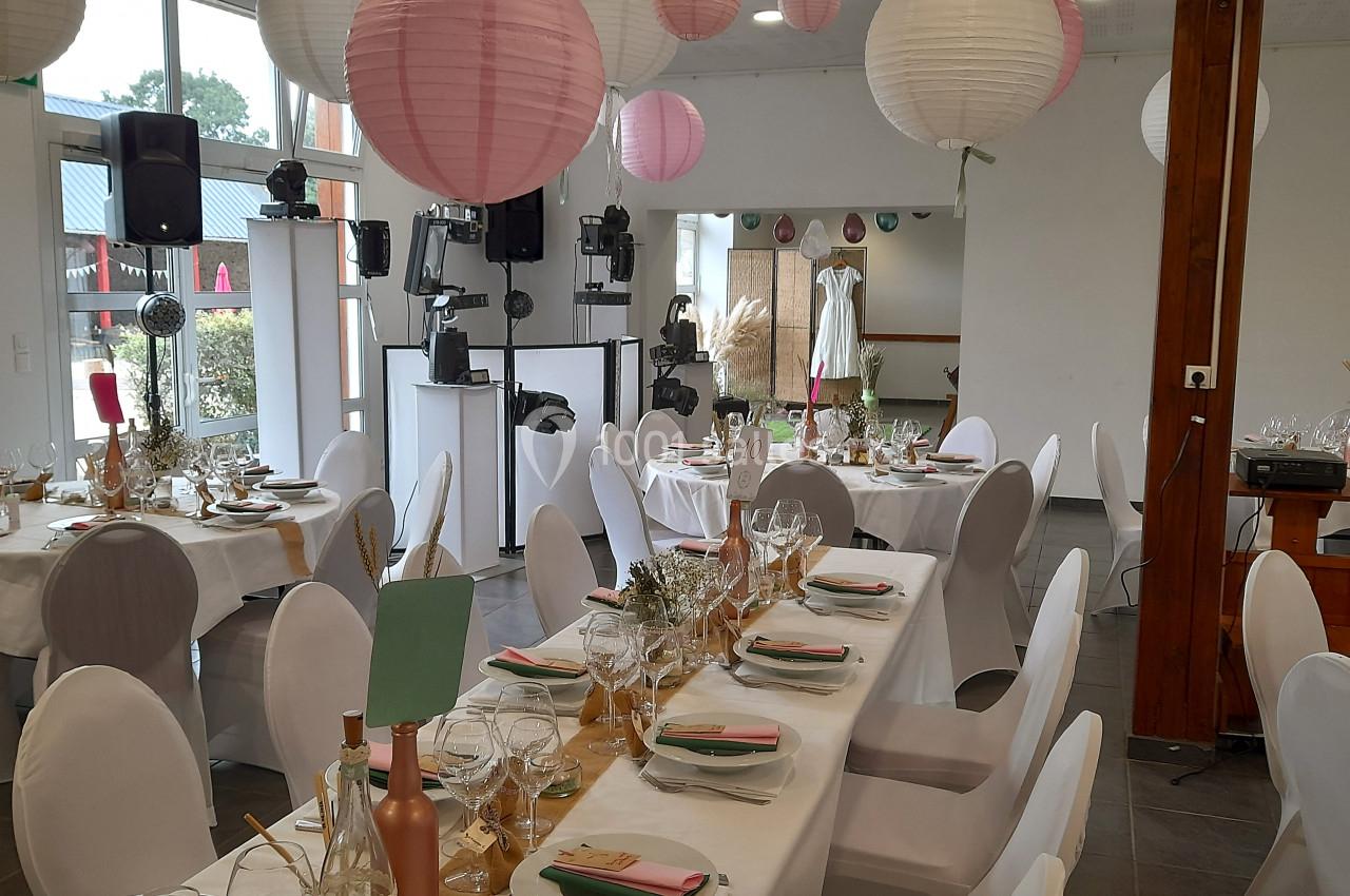 Salle décorée pour un événement avec des tables dressées, des lanternes suspendues et une robe exposée en arrière-plan.