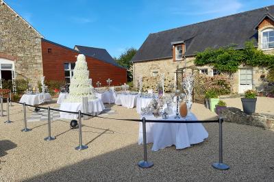 Table ronde décorée pour un événement, avec nappes beige, chaises blanches ornées de tissu orange et centre de table floral.