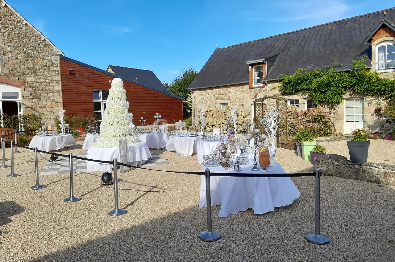 Cour extérieure avec tables décorées pour un événement, pièce montée blanche au centre, entourée de bâtiments en pierre.