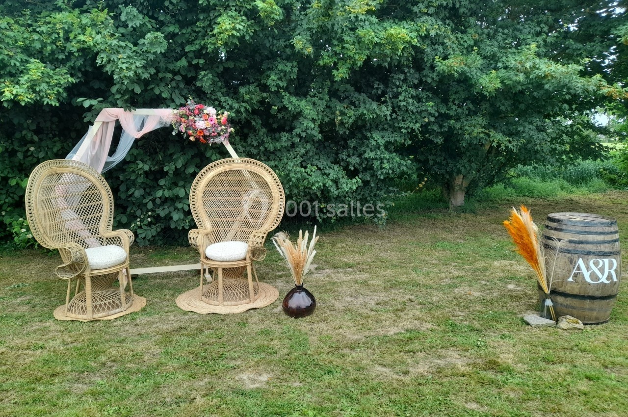 Deux fauteuils en rotin, un vase avec des herbes séchées et un tonneau décoratif dans un jardin verdoyant.