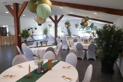 Table ronde décorée pour un événement, avec nappes beige, chaises blanches ornées de tissu orange et centre de table floral.