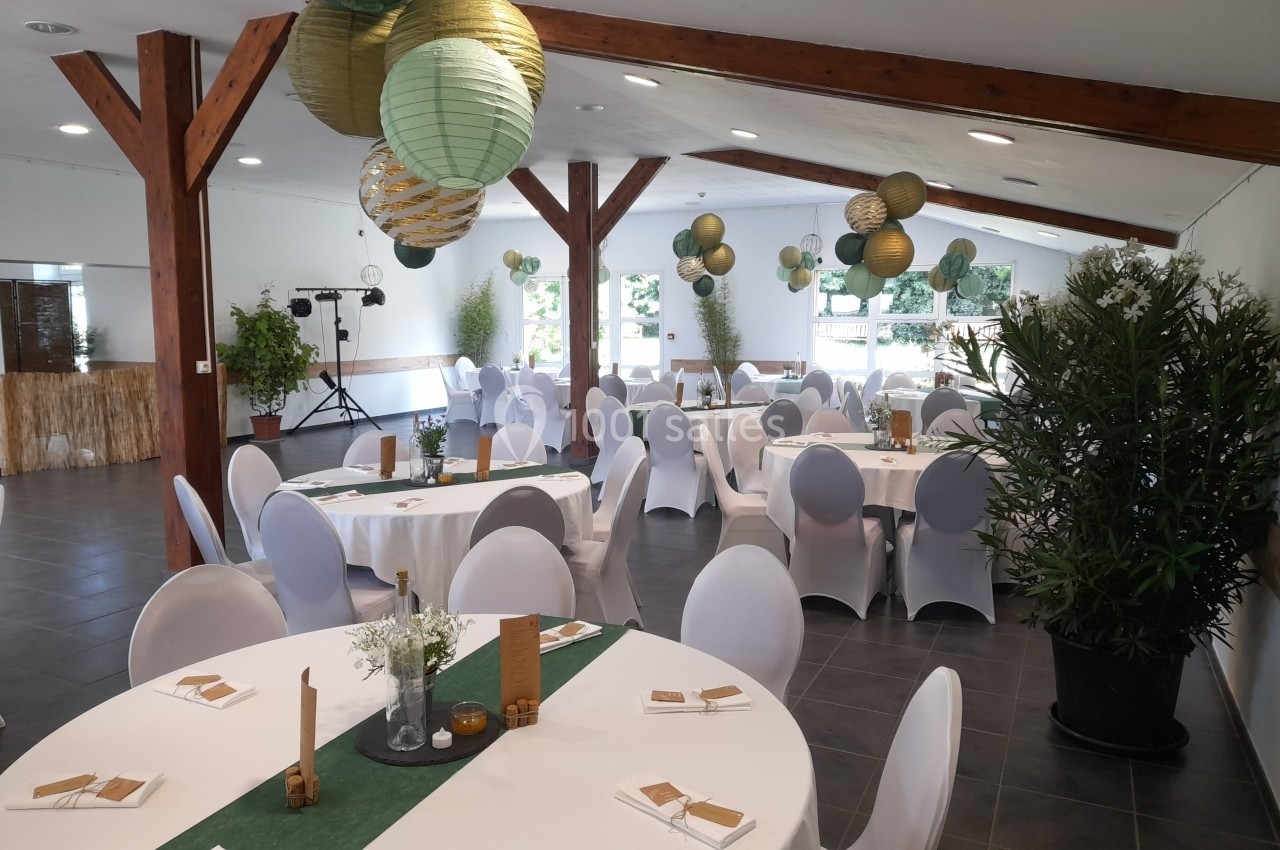Salle de réception décorée avec des tables rondes, nappes blanches, lanternes suspendues et plantes vertes.