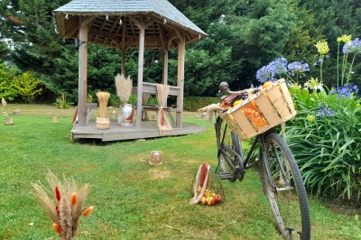 Table ronde décorée pour un événement, avec nappes beige, chaises blanches ornées de tissu orange et centre de table floral.
