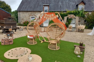 Table ronde décorée pour un événement, avec nappes beige, chaises blanches ornées de tissu orange et centre de table floral.