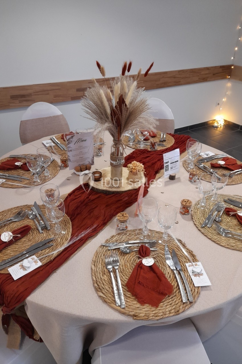 Table décorée pour un repas, avec nappes beige, chemins de table rouges, sets en osier et centre de table floral.