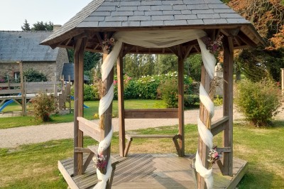 Table ronde décorée pour un événement, avec nappes beige, chaises blanches ornées de tissu orange et centre de table floral.