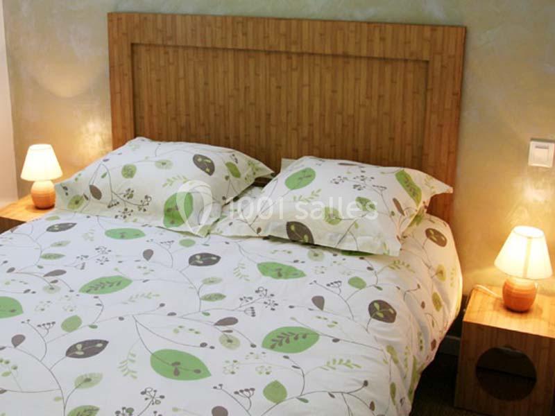 Lit double avec une parure à motifs végétaux, encadré par deux tables de chevet en bois avec lampes allumées.