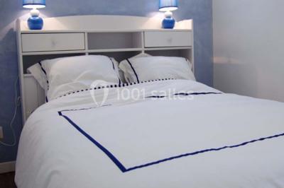 Lit double avec une parure à motifs végétaux verts et blancs, encadré par deux tables de chevet avec lampes allumées.