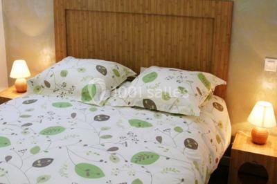 Lit double avec une parure à motifs végétaux verts et blancs, encadré par deux tables de chevet avec lampes allumées.