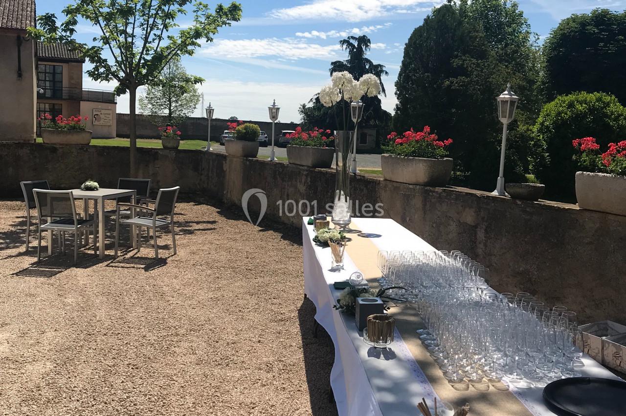 Table dressée avec verres et décorations sur une terrasse ensoleillée, entourée de végétation et de mobilier extérieur.