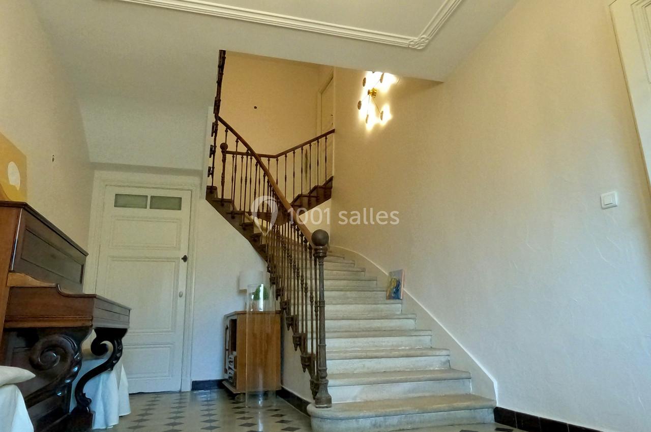 Escalier en bois avec rampe en fer forgé dans un hall lumineux au sol carrelé en motifs géométriques.
