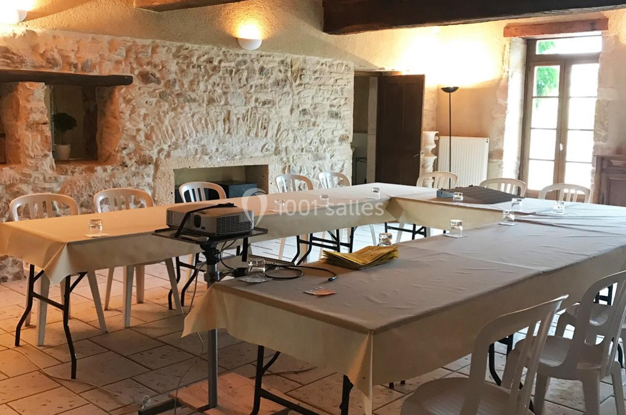 Salle de réunion lumineuse avec murs en pierre, tables rectangulaires couvertes de nappes et chaises en plastique.