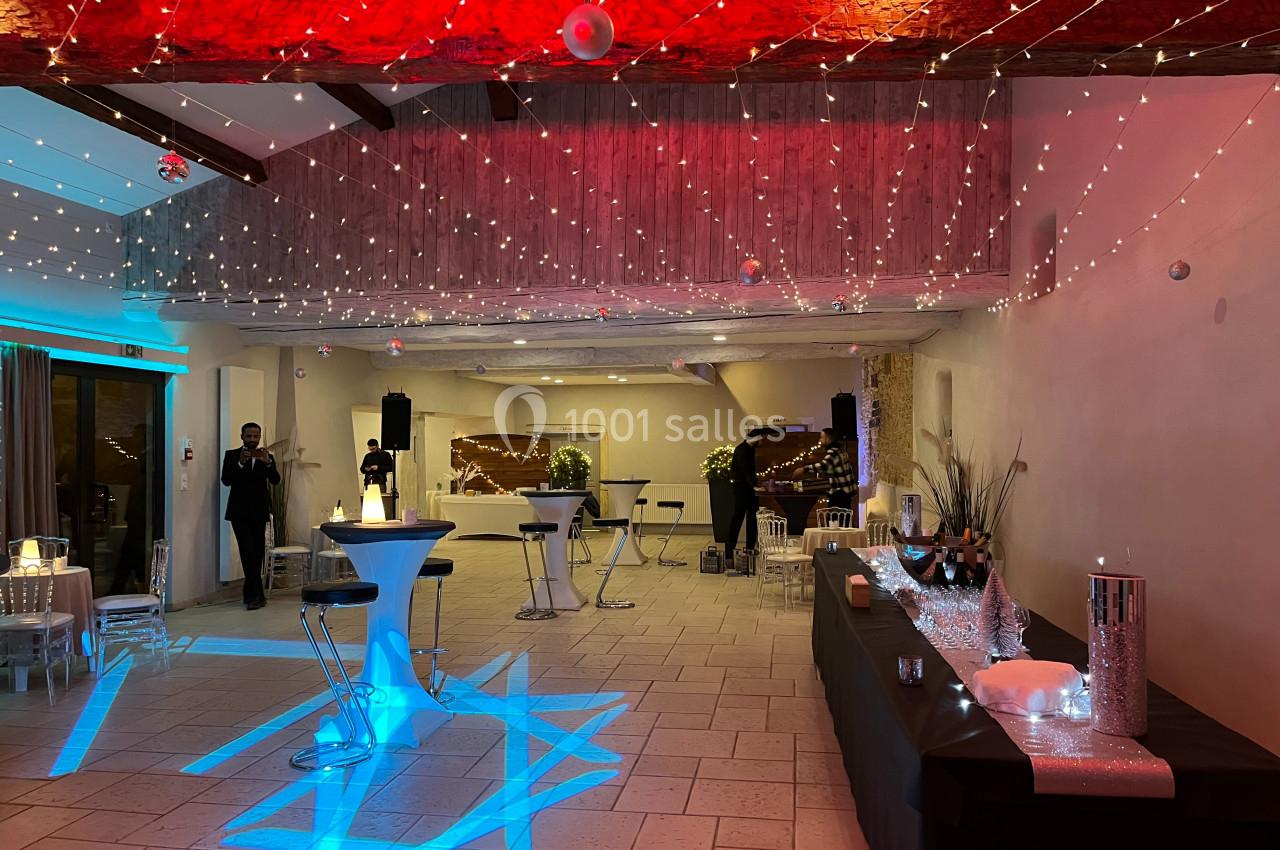 Salle de réception décorée avec des guirlandes lumineuses, tables hautes et buffet, ambiance festive et élégante.