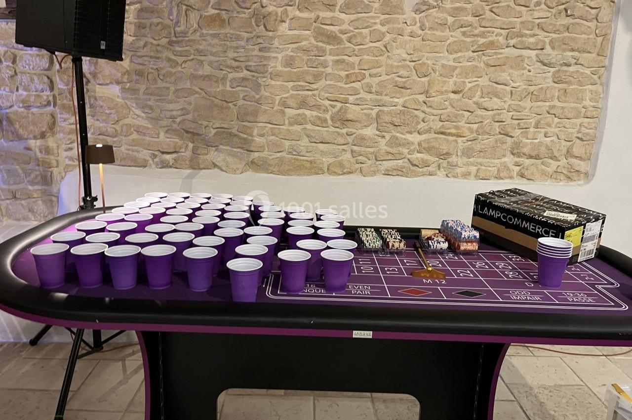Table de jeu avec des gobelets violets alignés, des jetons de casino et une boîte posée sur une nappe violette.