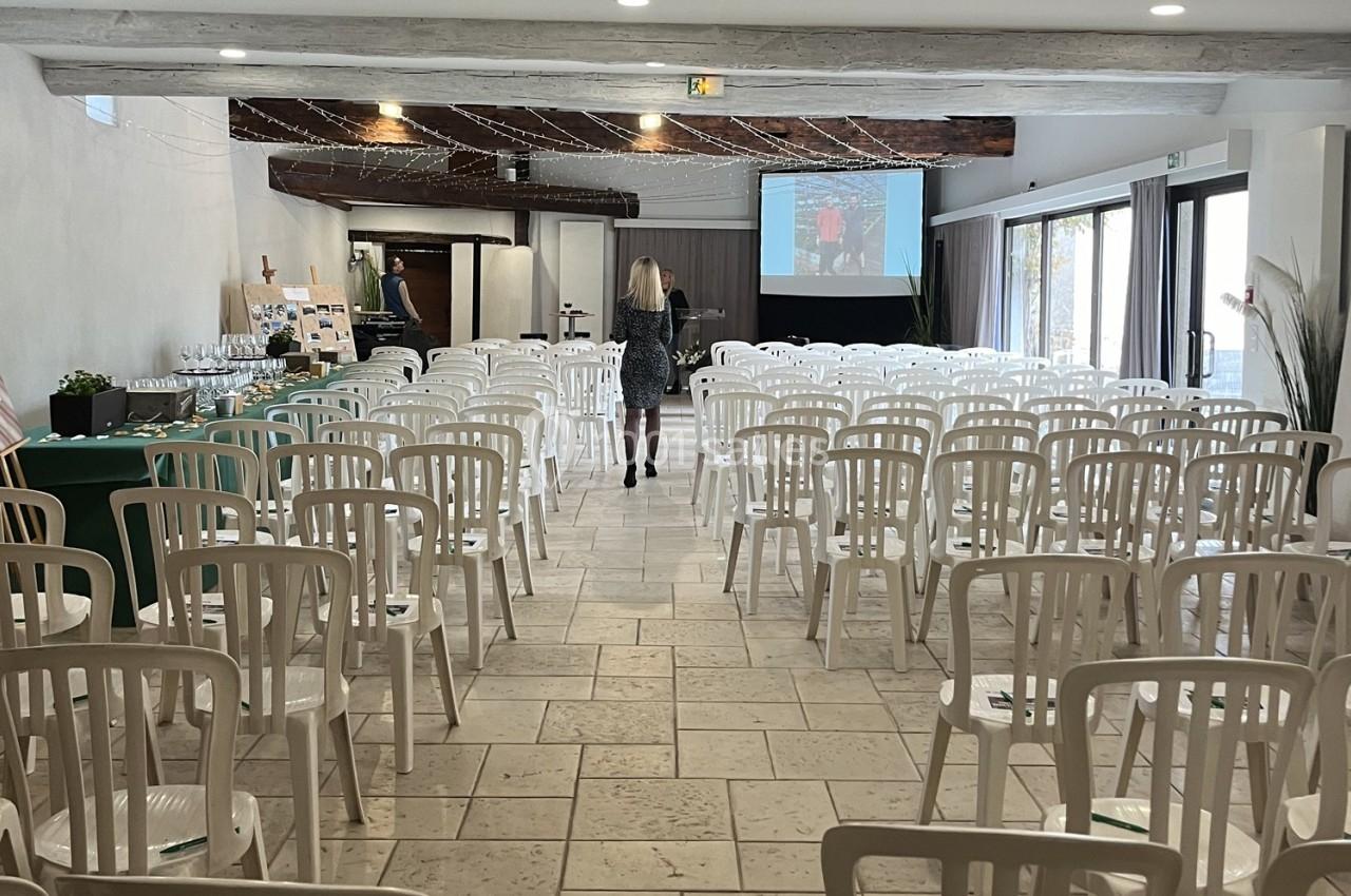 Salle de conférence lumineuse avec des chaises blanches alignées, un écran de projection et une table de réception.