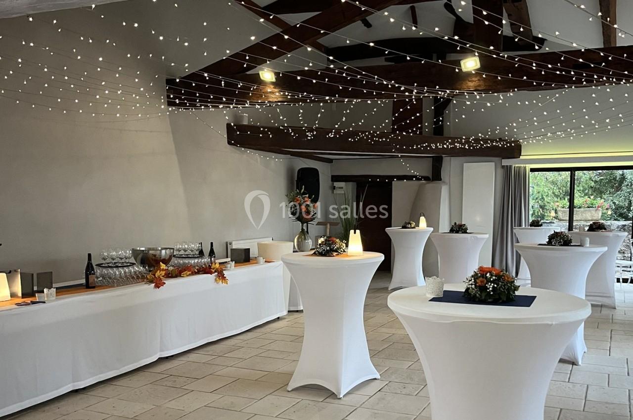 Salle de réception décorée avec des guirlandes lumineuses, tables hautes nappées de blanc et buffet dressé.