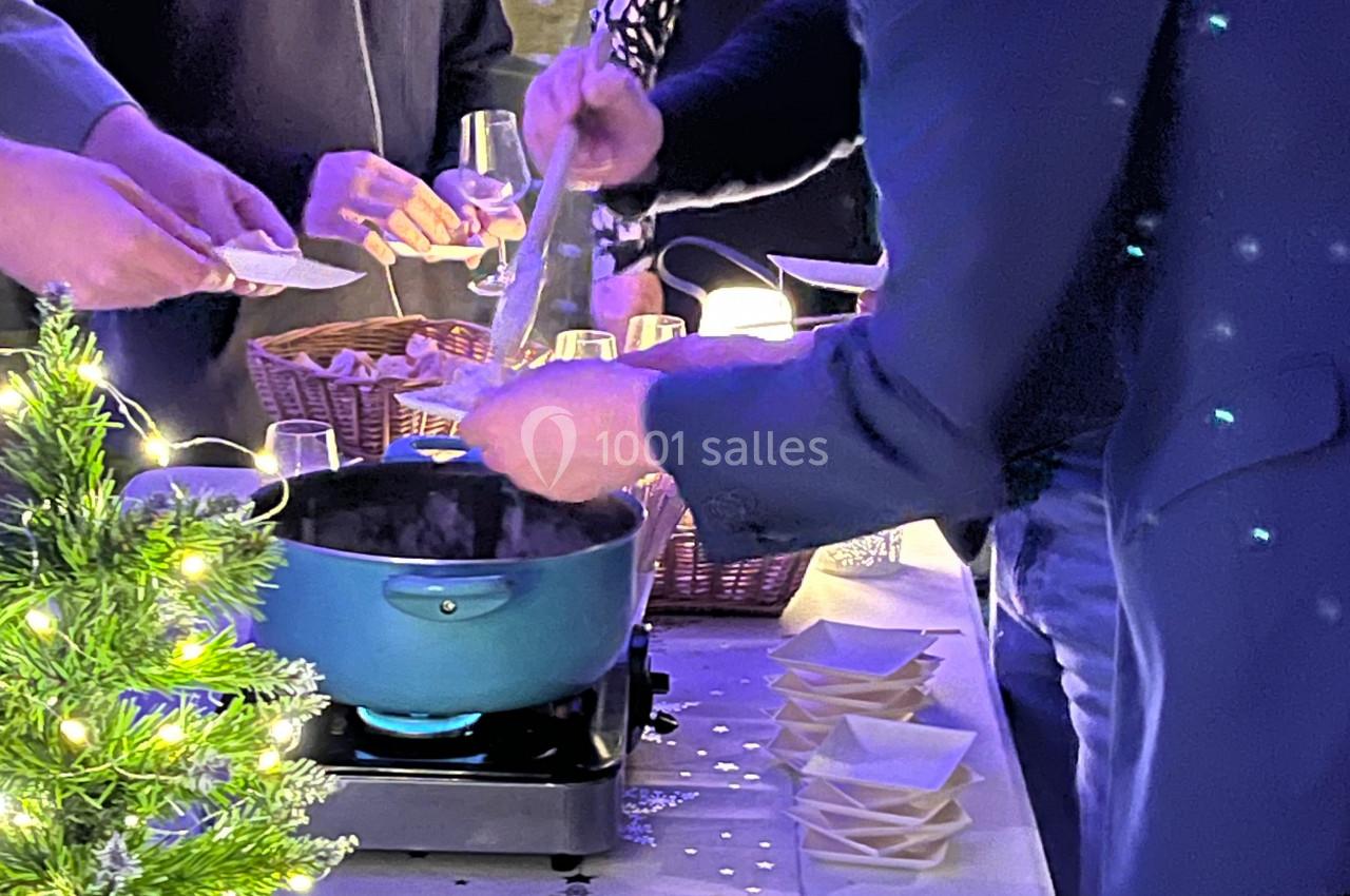 Un homme sert un plat chaud dans une ambiance conviviale, avec des tranches de charcuterie disposées sur une table éclairée.